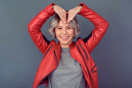 Young woman standing in leather jacket isolated on grey wall hands heart shapeの写真素材