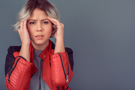 Young woman standing in leather jacket isolated on grey wall sickの写真素材