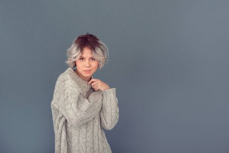 Young woman in a woolen sweater isolated on grey wall winter concept posingの写真素材
