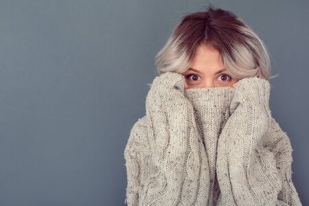 Young woman in a woolen sweater isolated on grey wall winter concept hidingの写真素材