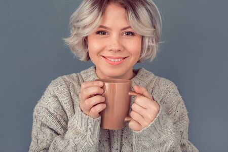 Young woman in a woolen sweater isolated on grey wall winter concept hot tea close-upの写真素材