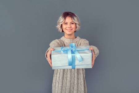 Young woman in a woolen sweater isolated on grey wall winter concept giving giftの写真素材