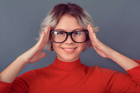 Young woman in a red blouse isolated on grey wall wearing eyeglassesの写真素材