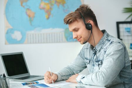 Young male travel agent consultant in tour agency writing documentsの写真素材