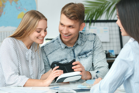 Young couple in a tour agency communication with a travel agent travelling concept holding virtual reality headsetの写真素材