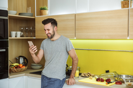 Bachelor man daily routine in the kitchen single lifestyle concept with phone smilingの写真素材