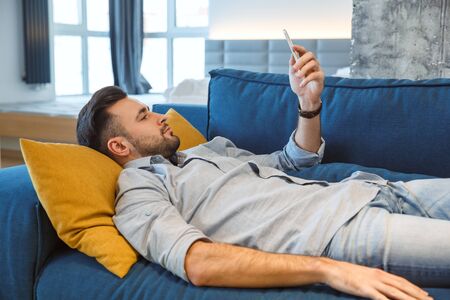 Bachelor man daily routine in the living room single lifestyle concept using smartphone tiredの写真素材
