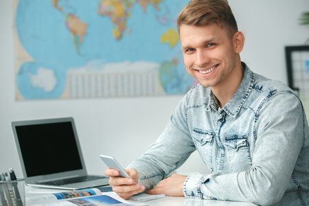 Young male travel agent consultant in tour agency holding smartphoneの写真素材