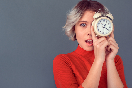 Young woman in a red blouse isolated on grey wall clock close-upの写真素材
