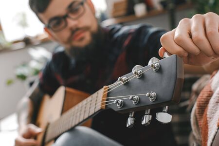 Young guitarist hipster at home with guitar fixing tuning pegs close-upの写真素材