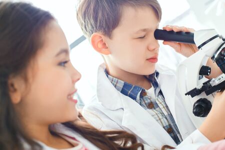 Little kids learning chemistry in school laboratory looking in a microscope close-upの写真素材