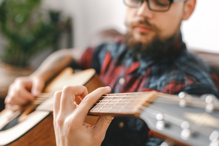Young guitarist hipster at home with guitar holding strings close-upの写真素材
