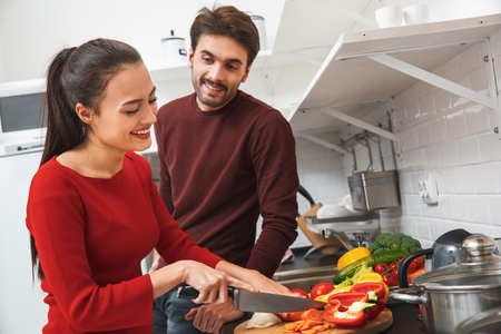 Young couple having romantic evening at home in the kitchen woman cutting vegetablesの写真素材