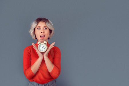 Young woman in a red blouse isolated on grey wall alarm clockの写真素材