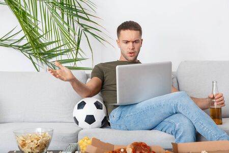 Young man sport fan watching soccer match on laptop irritatedの写真素材