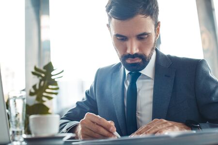 Businessman sitting in a business center restaurant writing documents close-up