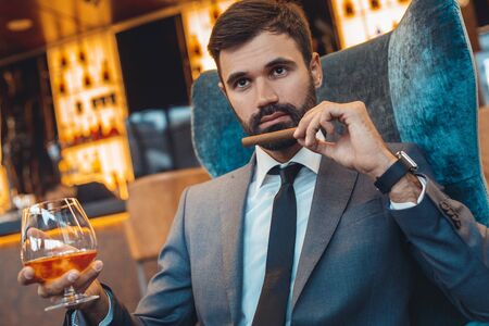 Businessman sitting in a business center bar smell the cigar close-upの写真素材