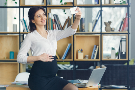 Pregnant business woman working at office motherhood taking selfie photosの写真素材
