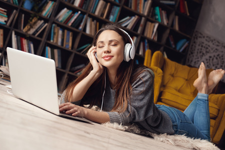 Young woman student in library at home lying listening favorite songの写真素材