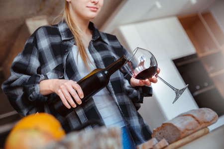 Young woman at home in the kitchen pouring wineの写真素材