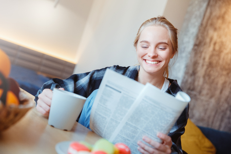 Young woman at home in the kitchen drinking tea reading newspaperの写真素材