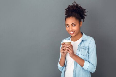 Young african woman isolated on grey wall studio casual daily lifestyle drinking coffeeの写真素材