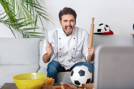 Young man chef sport fan watching match supporting teamの写真素材