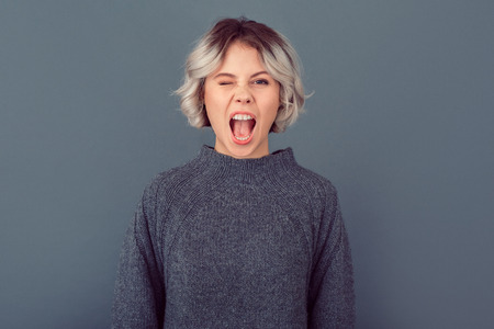 Young woman in a grey sweater studio picture isolated on grey background grimase winkの写真素材