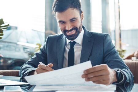 Businessman sitting in a business center restaurant signing documents happyの写真素材