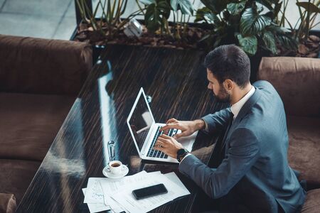 Businessman sitting in a business center restaurant typing on laptop top viewの写真素材