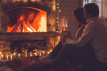 Young couple near the fireplace at home winter looking at flameの写真素材