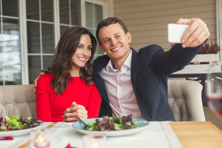 Young couple having romantic dinner in the restaurant sitting taking photosの写真素材