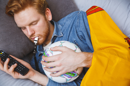 Man watching sport on tv at home alone sleeping close-upの写真素材