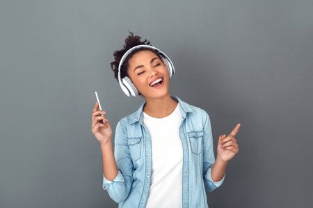 Young african woman isolated on grey wall studio casual daily lifestyle listening musicの写真素材