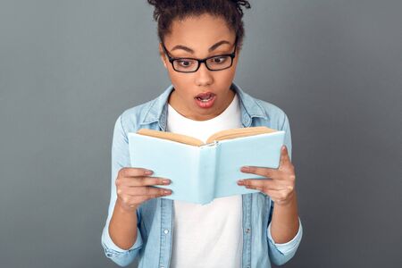 Young african woman isolated on grey wall studio casual daily lifestyle student reading book close-upの写真素材