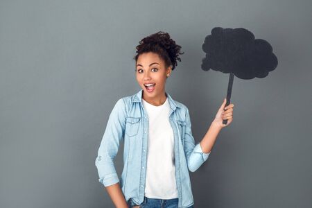 Young african woman isolated on grey wall studio casual daily lifestyle holfing cloud shaped paperの写真素材