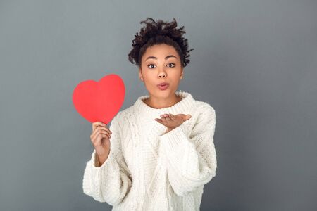 Young african woman isolated on grey wall studio winter concept air-kissの写真素材