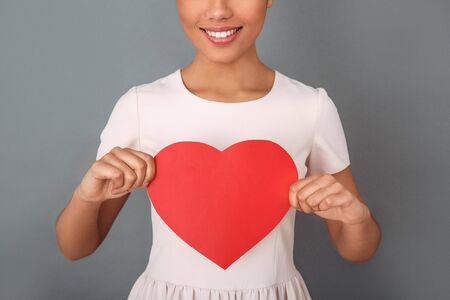 Young african woman isolated on grey wall studio celebration concept holding heart close-upの写真素材