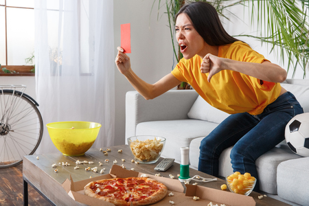 Young woman sport fan watching match in a yellow t-shirt ahowing red cardの写真素材