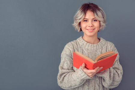 Young woman in a woolen sweater isolated on grey wall winter concept romantic novel bookの写真素材