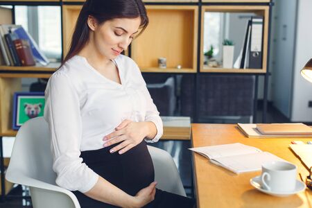 Pregnant business woman working at office motherhood sitting hugging bellyの写真素材
