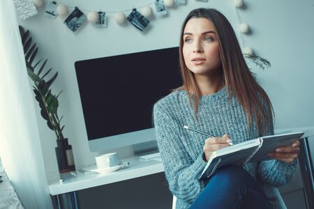 Young woman freelancer indoors home office concept casual style holding planner dreamingの写真素材