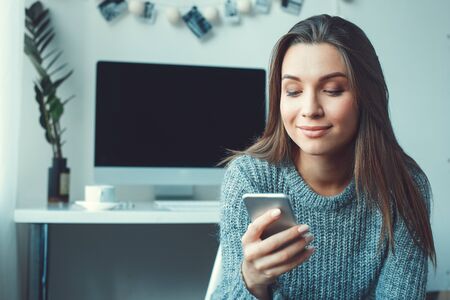 Young woman freelancer indoors home office concept casual style using smartphoneの写真素材