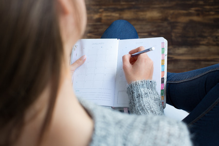 Young female freelancer at home office casual sitting writing in organizer back top view close-upの写真素材