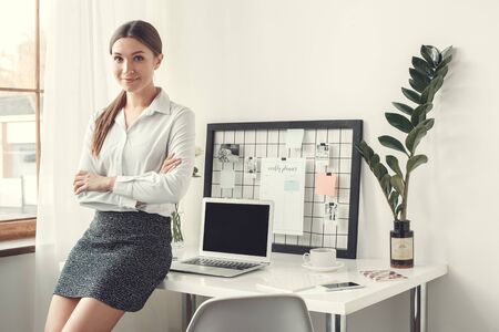 Young woman freelancer indoors home office concept formal style leaning on desk side viewの写真素材