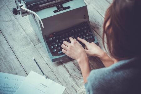 Young woman writer in library at home creative occupation typing typewriterの写真素材