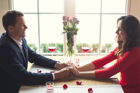 Young couple having romantic dinner in the restaurant sitting holding hands looking on each otherの写真素材