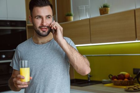 Bachelor man daily routine in a kitchen single lifestyle concept phone call drinking juiceの写真素材