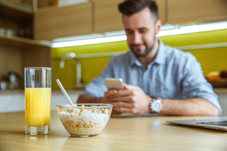 Bachelor man daily routine in the kitchen single lifestyle concept using smartphone during breakfastの写真素材