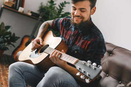 Young guitarist hipster at home with guitar sitting playing inspiredの写真素材